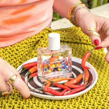 Small bottle of alcohol with colorful label on a plate with red chili peppers, held by a person with red nail polish.